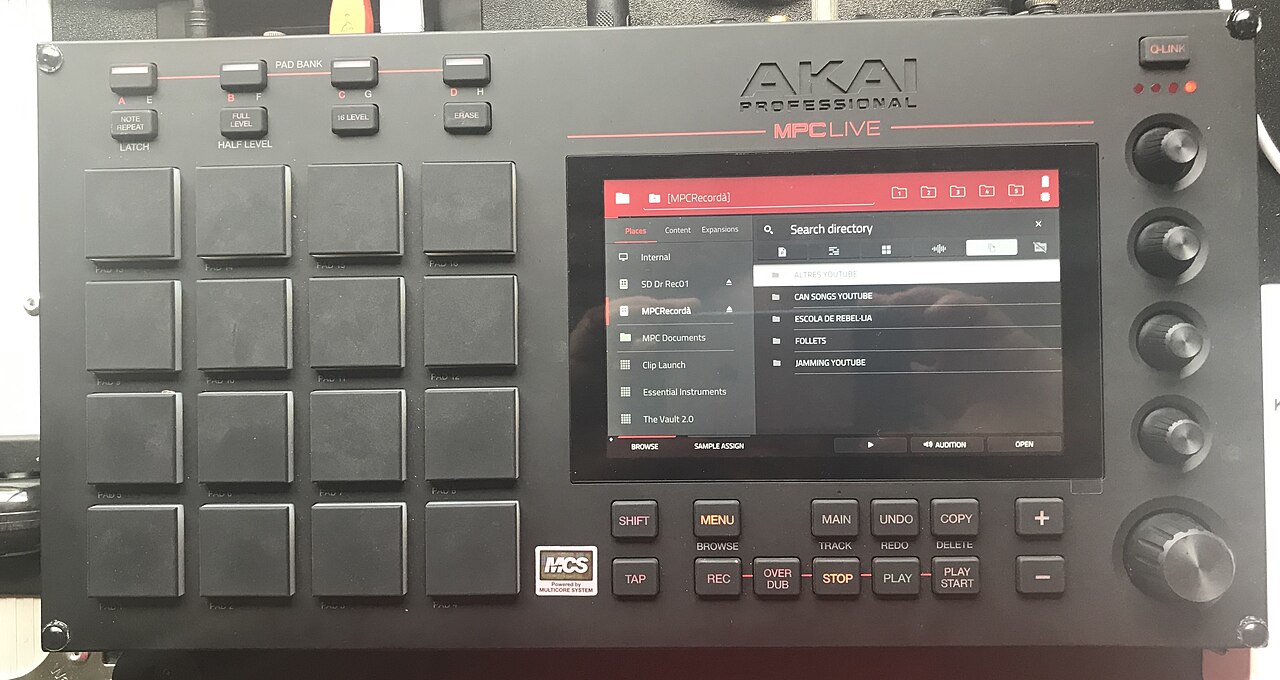 Top-down photograph of an Akai MPC Live standalone sampler showing its sixteen velocity-sensitive pads, touchscreen browser and Q-Link knobs — the hardware sampler workflow these gear terms describe.